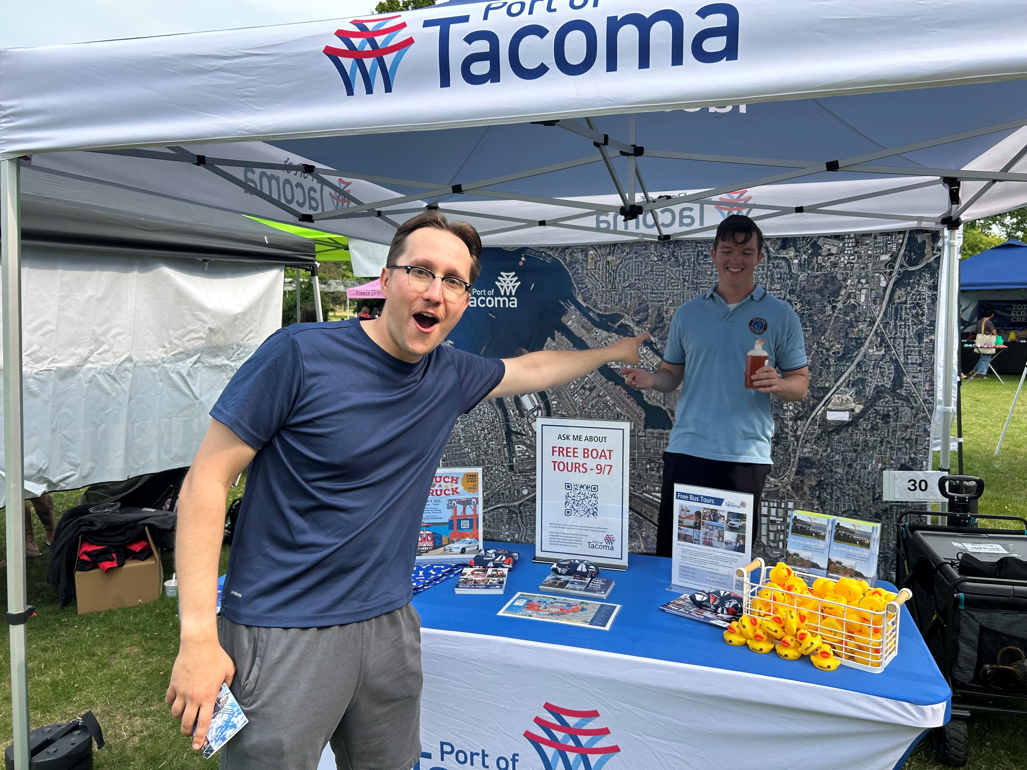 A man points at another man behind a table under a tent. 