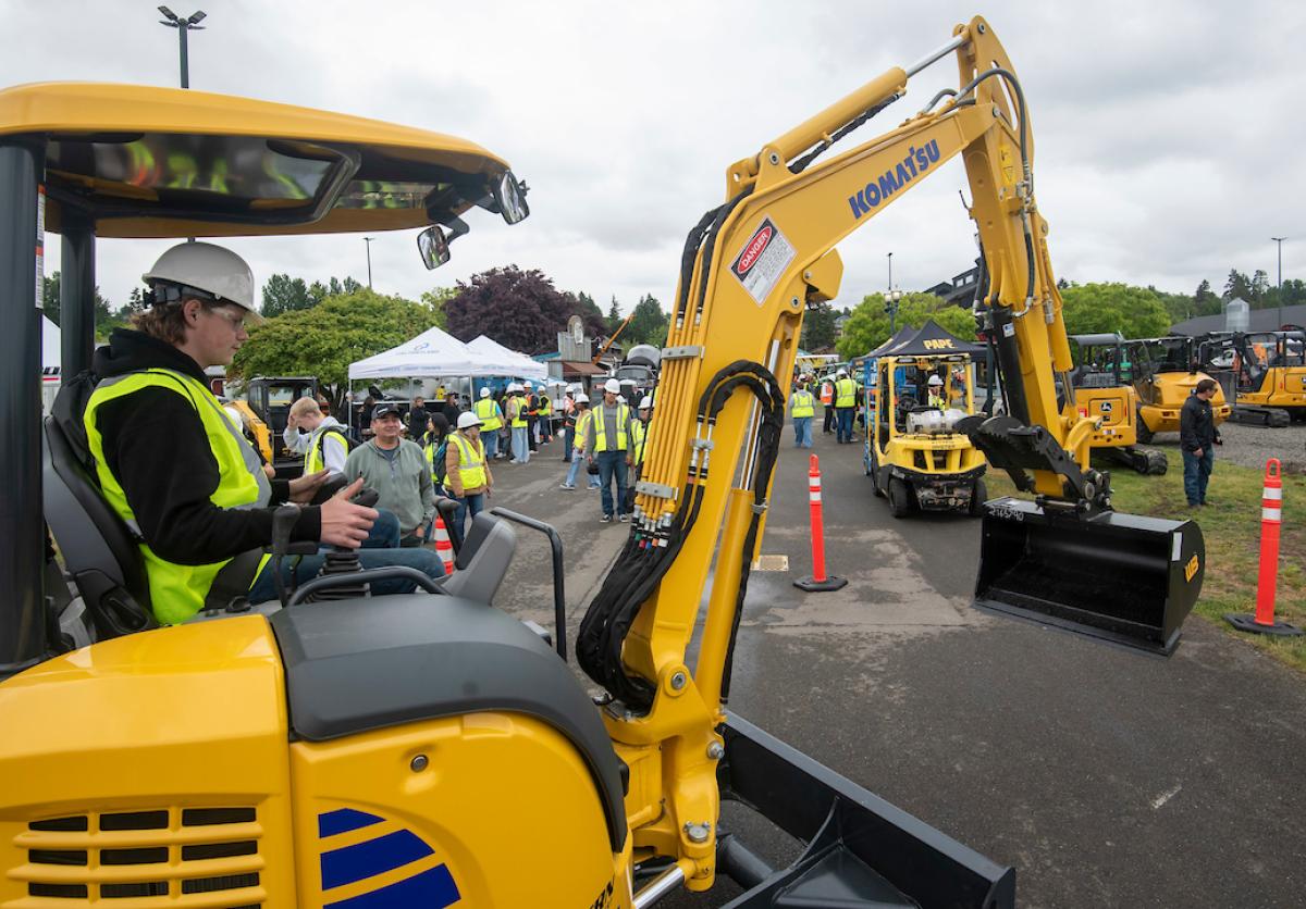 A student in protective gear sits in the cab of an excavator.